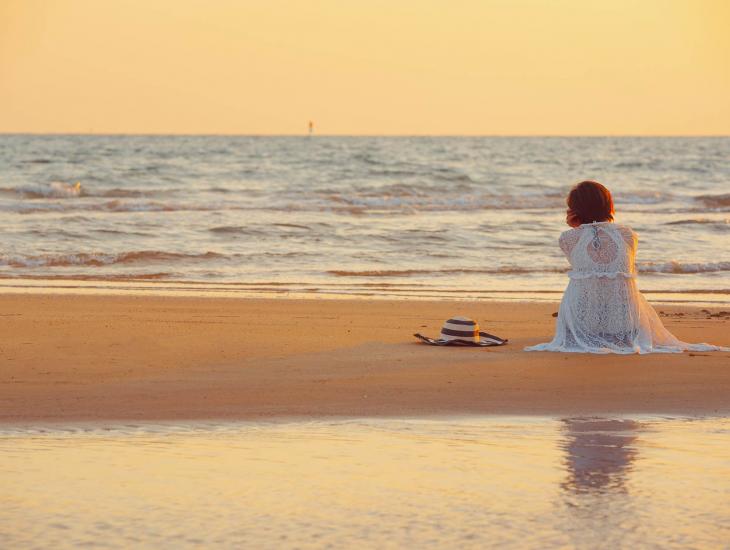 Een vrouw, op de rug gezien, zit op het strand bij zonsondergang