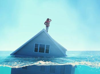 Een vrouw staat op het dak van een huis dat grotendeels onder water staat.