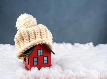Een miniatuurhuisje in de sneeuw, met een wollen mutsje op