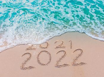 De jaartallen 2021 en 2022, geschreven in het natte zand op de vloedlijn van het strand