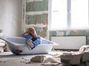 Jonge vrouw zit in een losse badkuip die in een gestripte badkamer ligt